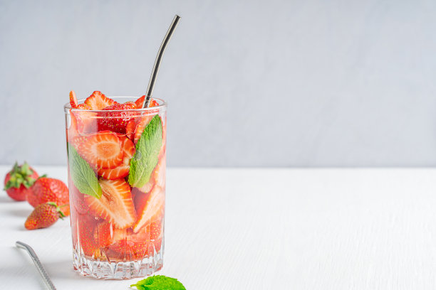 一杯冷排毒浸泡水制成的草莓和薄荷叶与稻草在白色的木制背景与拷贝空间图片下载