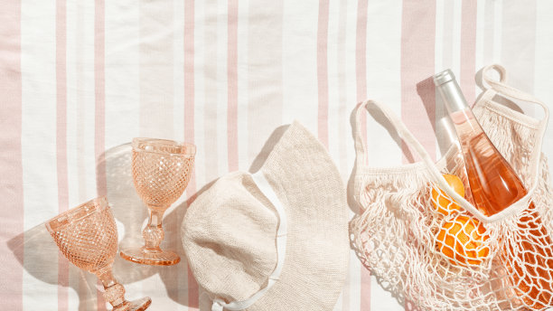 夏天最小的平面宽檐帽，葡萄酒杯，瓶玫瑰酒，橙色水果在条纹沙滩毛巾为背景，阳光的阴影。夏天粉彩审美照片。图片下载