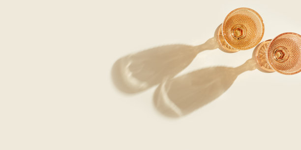 白葡萄酒酒杯桃色玻璃在米色的背景与黑暗的阴影，从太阳眩光。最小夏季休息的概念。干葡萄酒在彩色玻璃器皿高脚杯风格。创造性的俯视图图片下载