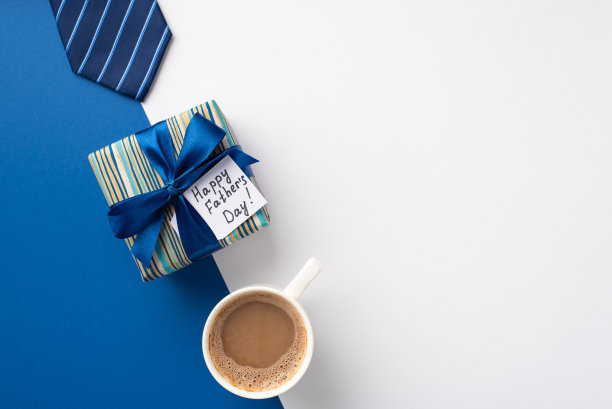父亲节的概念。顶视图照片的时尚礼品盒的缎带蝴蝶结和明信片蓝色领带和咖啡杯双色蓝色和白色的背景与copyspace图片下载