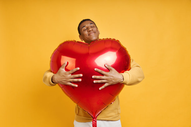 英俊的混血男子拥抱大的心形气球图片下载