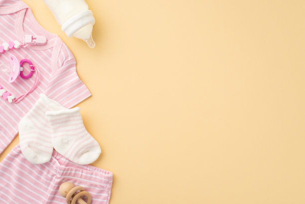 婴儿服装的概念。顶视图照片的粉红色衬衫内裤袜子奶嘴链瓶和木制拨号鼓孤立粉彩米色背景与copyspace图片下载