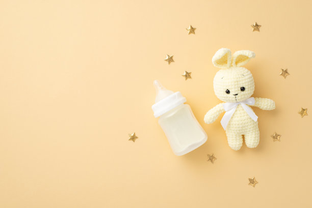 小配件的概念。顶视图的针织兔玩具奶瓶和金色的星星在孤立粉彩米色背景与copyspace图片下载