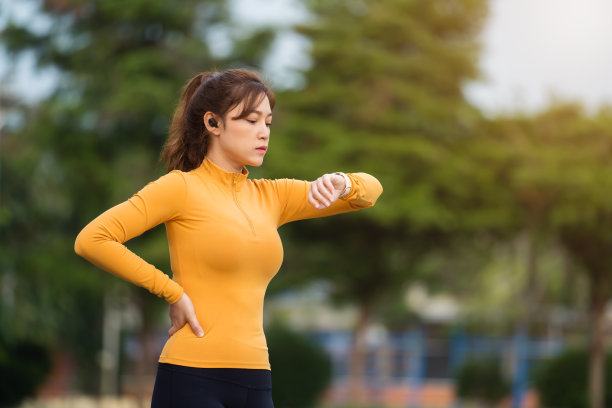 年轻女子跑步，看着她的智能手表在公园图片下载