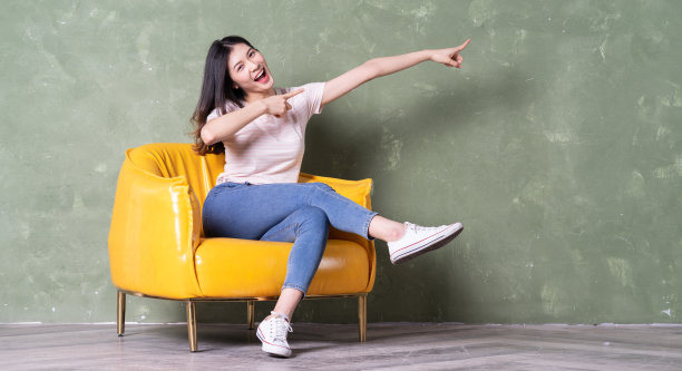 年轻漂亮的亚洲女人坐在黄色扶手椅上的形象图片下载