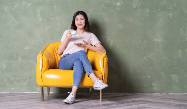 年轻漂亮的亚洲女人坐在黄色扶手椅上的形象图片下载