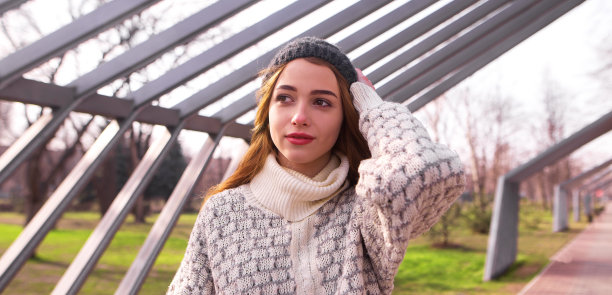 户外照片美丽的女孩长头发穿着针织毛衣和帽子，在春天公园摆姿势图片下载