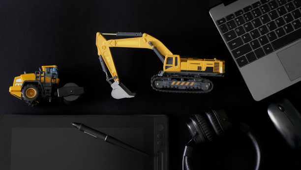 触控笔和图形平板电脑，电脑鼠标，笔记本电脑和耳机在黑色旁边的模型挖掘机和沥青压路机。Ð建筑设备及园林绿化工程设计理念图片下载