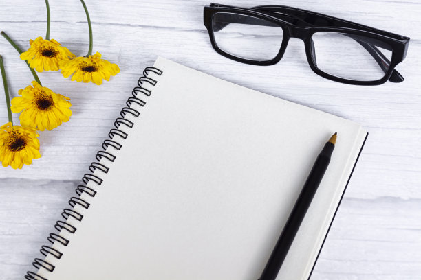 记事本平放着向日葵，老花镜和笔在木桌上。图片下载