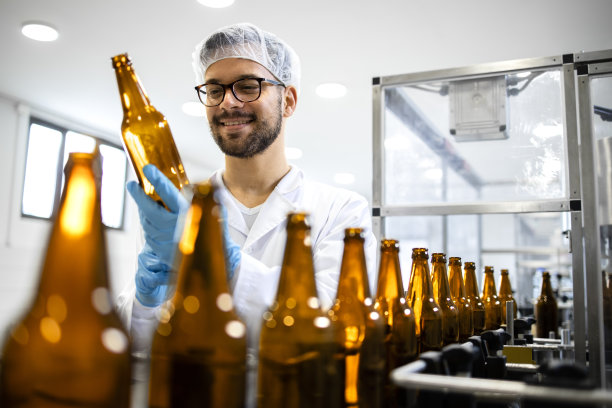 饮料装瓶厂和技术工人在装酒前检查啤酒瓶。图片下载