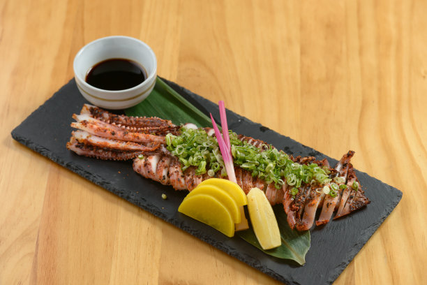 日本食物烤牛肉干与柠檬和酱油在一个黑色的盘子孤立在木制桌子上俯瞰图片下载