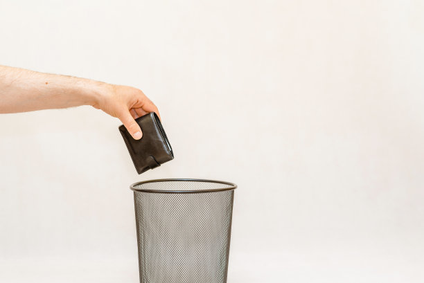 黑色钱包被扔进垃圾桶，可以进行处理和回收。白色，灰色背景，选择性聚焦，复制空间。图片下载