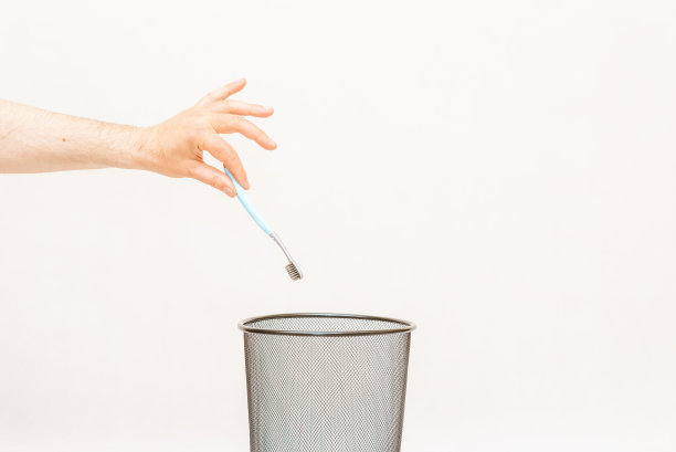 牙刷被扔进了垃圾桶。白色，灰色背景，选择性聚焦，复制空间。图片下载