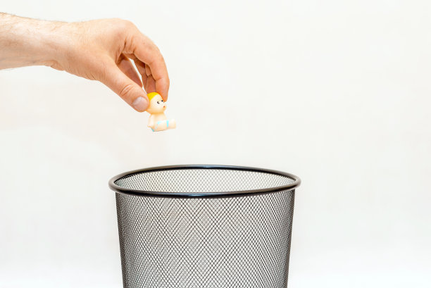 微型玩具婴儿，婴儿被扔进垃圾桶。白色，灰色背景，选择性聚焦，复制空间。图片下载