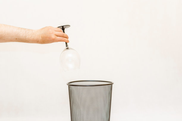 一杯酒被扔进垃圾桶，可以进行处理和回收。白色，灰色背景，选择性聚焦，复制空间。图片下载