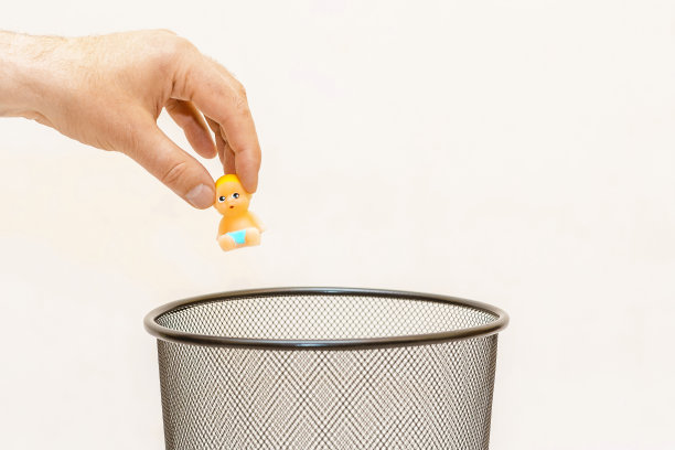 微型玩具婴儿，婴儿被扔进垃圾桶。白色，灰色背景，选择性聚焦，复制空间。图片下载