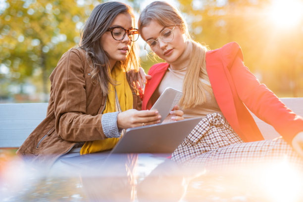 两个女性朋友在秋季公园用手机图片下载