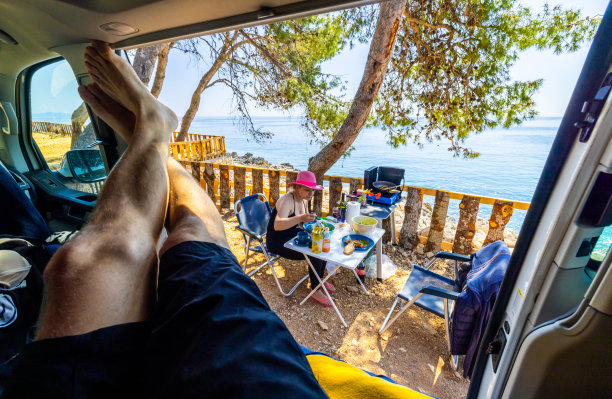 男人在露营车里放松，而女人坐在椅子上吃海上食物图片下载