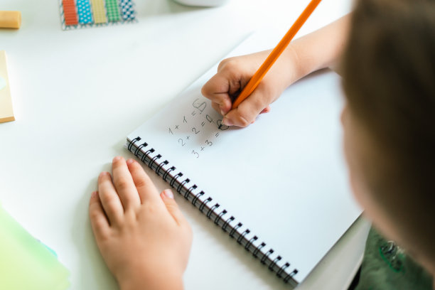 远程学习在线教育。小男孩在家看书，在笔记本上写东西，做家庭作业。孩子拿着记事本坐在桌子旁。解决数学问题。回到学校图片下载