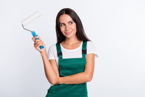 迷人的女士抱着画家滚筒的照片看空穿绿色整体孤立的白色背景图片下载