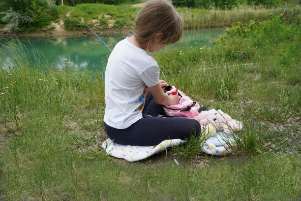 一个7-8岁的小女孩坐在河边玩玩具。图片下载