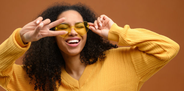 多种族美丽随和的惊人的女士显示v标志近眼与她的手说嗨孤立的棕色图片下载