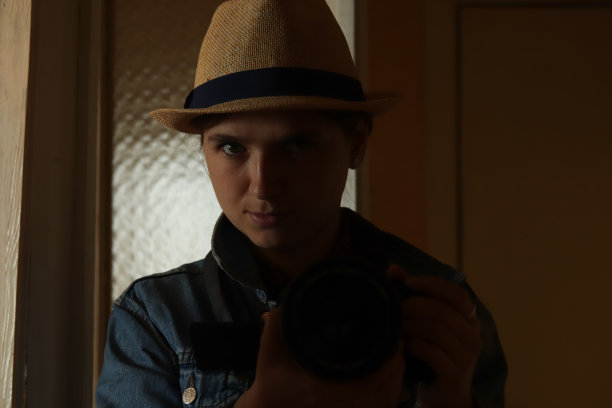 散焦的年轻女子在镜子反射摄影。戴帽子的千禧一代女性。深黑的肖像。心理健康。自恋。严肃的摄影师。的焦点图片下载