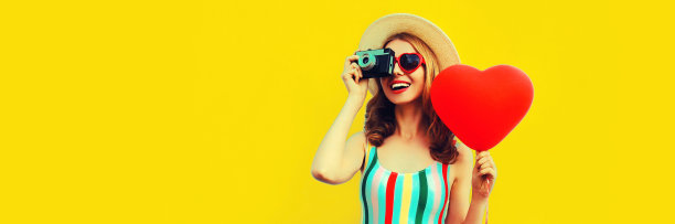 夏天的肖像快乐微笑的年轻女子与电影相机和红色的心形气球戴着草帽在黄色的背景，空白的拷贝空间的广告文字图片下载