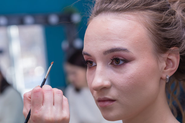化妆师的手和刷子靠近女孩的脸在沙龙。图片下载