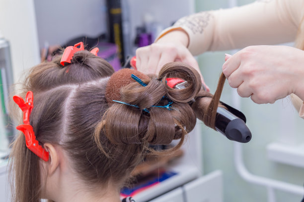 手握卷发棒的师傅把一缕头发卷上特写。图片下载