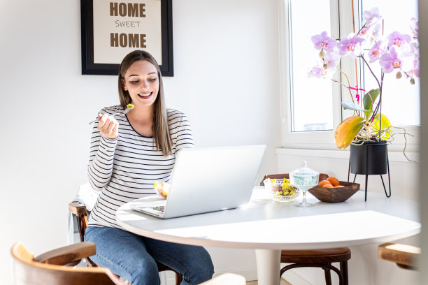 孕妇坐在家里的桌子上用笔记本电脑进行视频通话。图片下载