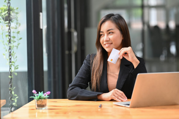 微笑的年轻亚洲女性持有信用卡和使用笔记本电脑银行或网上购物。图片下载