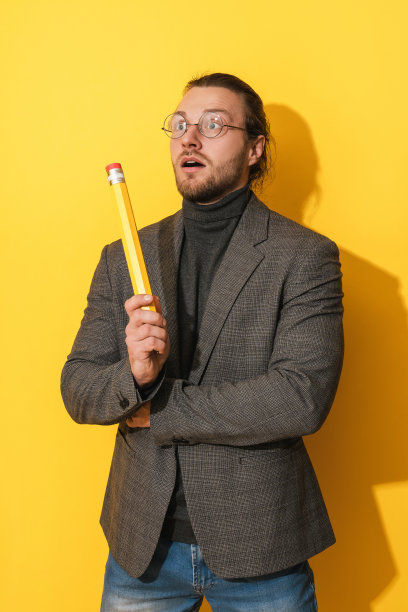 有灵感的男人戴着眼镜，拿着黄色背景上的大铅笔图片下载