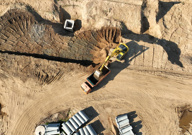 挖掘机将沙子装入自卸卡车。建筑工地的土方工程。为下水道施工和卫生下水道挖地。挖掘机用自卸车装砂。建筑工地的土方工程。为下水道施工挖地图片下载