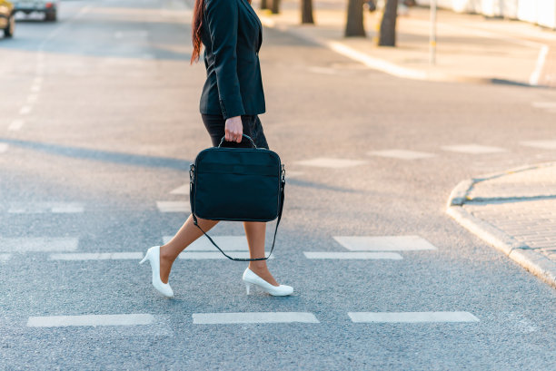 腿部细节的商务女性在去办公室的路上，走在户外，拿着笔记本电脑，穿着商务套装和高跟鞋。裁剪的看法，商业妇女走在城市。复制空间，腰部以下。图片下载