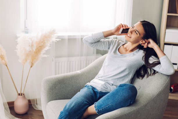 一个年轻的女孩正在讲手机，坐在椅子上，用她的脚爬到椅子上图片下载