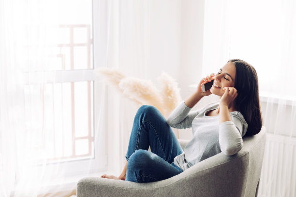 一个年轻的女孩正在讲手机，坐在椅子上，用她的脚爬到椅子上图片下载