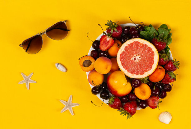 新鲜水果和浆果与太阳镜，海贝和海星在明亮的黄色背景图片下载
