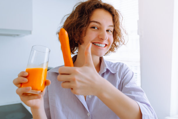 年轻女子微笑着向家里厨房里的超级新鲜胡萝卜竖起大拇指图片下载