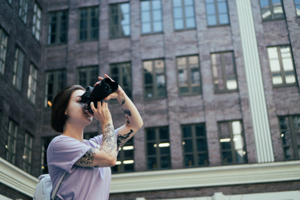 年轻女孩摄影师拍摄城市建筑。纹身女孩拿着相机在市中心拍照图片下载