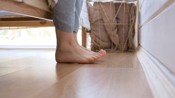 一个漂亮姑娘的腿从床上爬起来靠在窗户上。光的背景，早晨醒来。白床美女脚趾。到地板上去。镶木地板或层压板。健康的腿图片下载