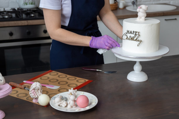 戴着手套的手擦拭基底，基底上有现成的蛋糕，上面写着“生日快乐”。桌上有工具和糖果。有选择性的重点。关于糖果商、食物、爱好的照片。图片下载