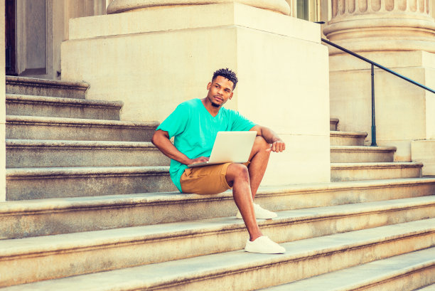年轻人在笔记本电脑上工作，坐在纽约办公楼外的楼梯上图片下载
