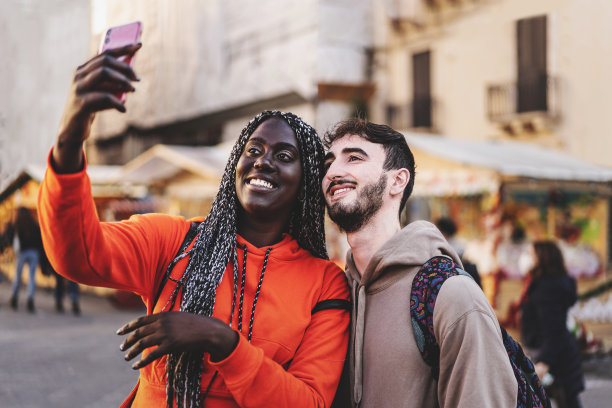 一对跨种族的年轻人在城市市场自拍，游客们在一起拍照图片下载