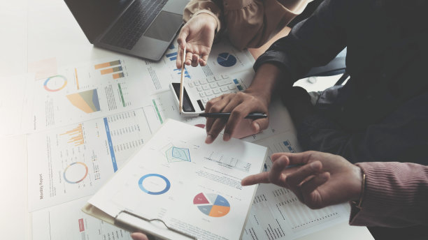 商务人士开会时使用笔记本电脑、计算器、笔记本、股票行情图纸进行分析，计划下月提高质量。企业理念图片下载