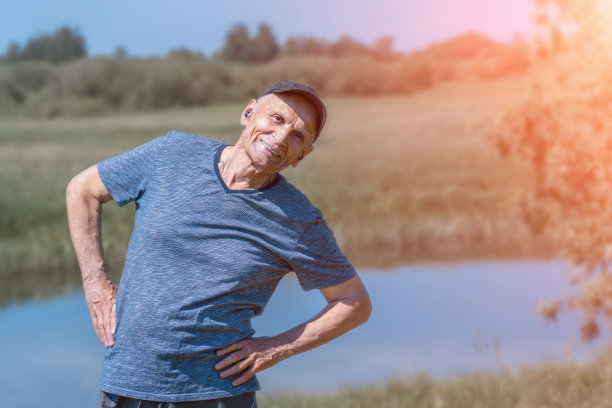 一个戴着耳机戴着帽子的老人在河边锻炼。图片下载