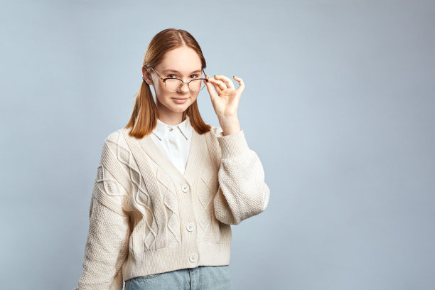 可爱的学生女孩穿着米色毛衣，戴着时髦的眼镜微笑着，在大学早上的讲座后休息。图片下载