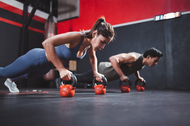 运动的年轻情侣在健身房做着壶球上的俯卧撑。强大的综合健身锻炼。图片下载