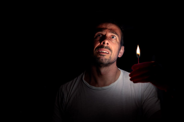 在黑暗中，一个拿着火柴的担心的人抬头看。中断的概念。图片下载