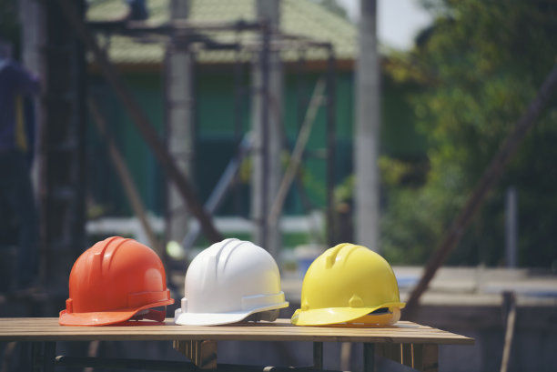 工程师、安全员或建筑师戴的安全帽，请放在水泥地上。施工现场黄色、白色、橙色安全帽(安全帽)。图片下载